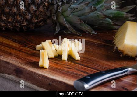 Ananasscheiben auf einem Holzschneidebrett mit einer ganzen Ananas im Hintergrund Stockfoto