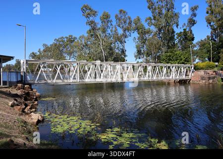 Eine Fußgängerbrücke aus Metall überquert das Wasser mit Seerosenflächen und Bäumen in der Hoods Lagoon in Clermont, Queensland, Australien Stockfoto