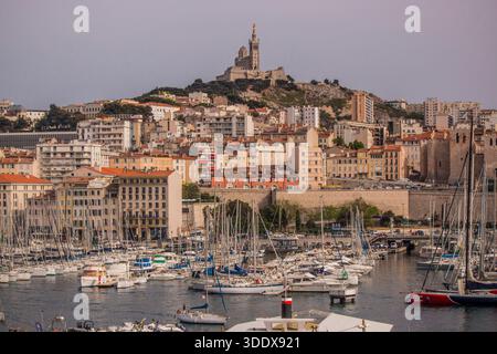 Sonnenuntergang über dem Vieux-Port mit Booten im Yachthafen und der Basilika Notre-Dame de la Garde auf dem Hügel unter einem violetten Himmel, Marseille, Frankreich. Stockfoto