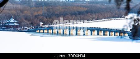 Touristen laufen über die Seventeen Arch Bridge am Sommerpalast in Peking, während der Kunming See gefroren und mit Schnee bedeckt liegt. Stockfoto
