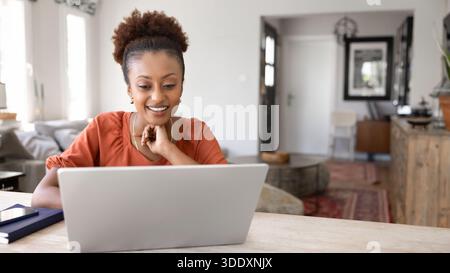 Positive junge afroamerikanische freischaffende Frau, die am Laptop arbeitet Stockfoto