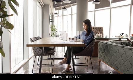 Positive junge asiatische Managerin, die am Desktop im Büro arbeitet Stockfoto