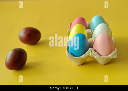 Bunte Ostereier im Karton auf gelbem Hintergrund Stockfoto