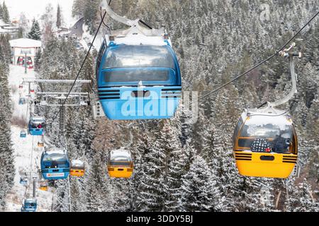 Ruzomberok, Slowakei - 4. Januar 2025: Farbenfrohe Gondeln der Skilifte, die sich während der Wintersaison über schneebedeckten Wald im Malino Brdo Resort bewegen Stockfoto