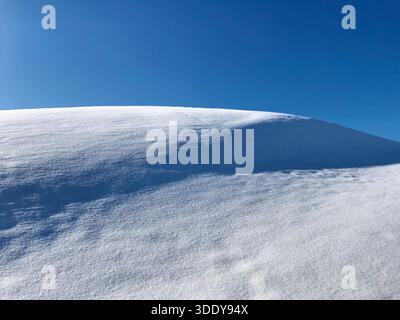 Einzigartige Winterszene mit einem sanft abfallenden Hügel, der von unberührtem Schnee bedeckt ist, mit langen Schatten der Sonnenstrahlen, die starke natürliche Kontraste erzeugen Stockfoto