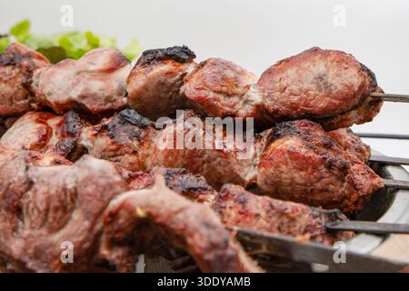 Gegrillte Fleischstücke auf Metallspießen mit Salat auf hellem Hintergrund, Seitenansicht Stockfoto