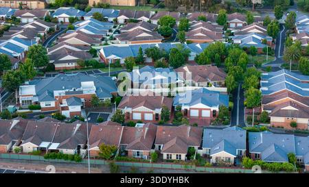 Eine erhöhte Perspektive fängt eine weitläufige Vorstadtlandschaft mit zahlreichen Häusern mit kontrastierenden Dachfarben, grünen Bäumen und gewundenen Straßen ein Stockfoto