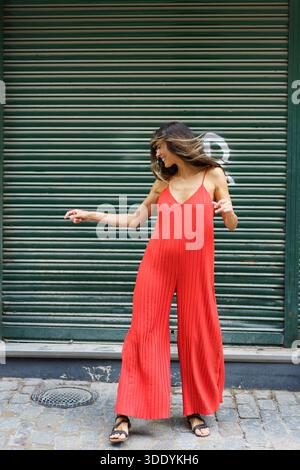 Eine stilvolle Frau in einem leuchtenden roten Jumpsuit posiert selbstbewusst vor einem grünen Hintergrund Stockfoto
