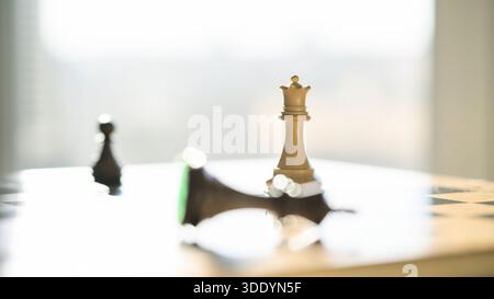 Eine stehende Schachkönigin ist scharf im Fokus, während ein gefallener König unscharf im Vordergrund auf einem Schachbrett liegt. Stockfoto