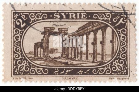 SYRIEN - 1. März 1925: 2 dunkelbraune Briefmarken aus der Zeit des französischen Mandats mit Blick auf Tadmur, Säulenstraße und Triumphbogen, die monumentalen Ruinen von Palmyra, einer antiken Oasenstadt in der syrischen Wüste. Die ikonischen Säulenbögen und Bögen aus der römischen Ära bestimmen den Ort, der auch unter seinem aramäischen Namen Tadmor bekannt ist. Der Rahmen ist mit geometrischen Mustern und floralen Motiven verziert, die typisch für die Kunst dieser Zeit sind. Historisch gesehen war 1925 ein bedeutendes Jahr für Syrien, da damals der große syrische Aufstand gegen die französische Kolonialherrschaft begann Stockfoto