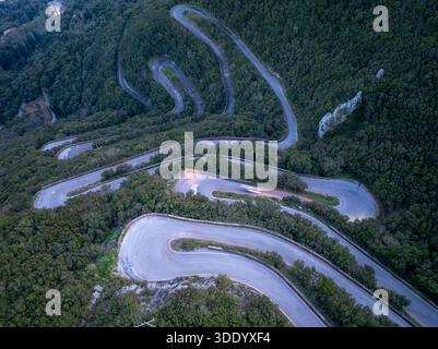 Aus der Vogelperspektive auf die gewundene Bergstraße mit Haarnadelkurven und leichten Wegen in der Abenddämmerung in Sokraki, Korfu, Griechenland Stockfoto