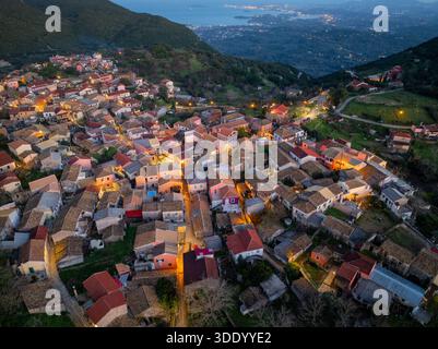Panoramablick auf das beleuchtete traditionelle Bergdorf Sokraki in der Abenddämmerung mit fernen Küstenlichtern und Blick auf das Ionische Meer, Korfu isla Stockfoto