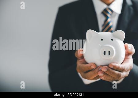 Nahaufnahme der Hände eines Geschäftsmannes, der eine weiße Schweinebank hält. Der Geschäftsmann trägt einen Anzug und Stockfoto