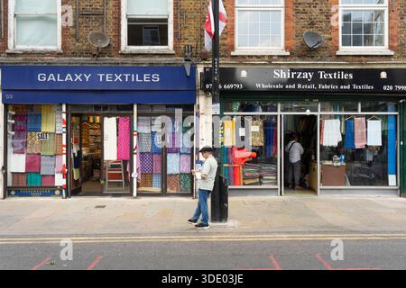 Ein Mann steht vor Galaxy Textiles in der Wentworth Street, Aldgate London, und durchsucht Stoffe. Stockfoto