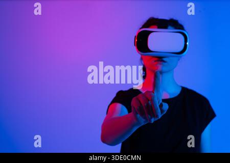Nahaufnahme einer Frau mit Virtual-Reality-Headset und berührender virtueller Schnittstelle mit dem Finger in futuristischer Neonbeleuchtung Stockfoto