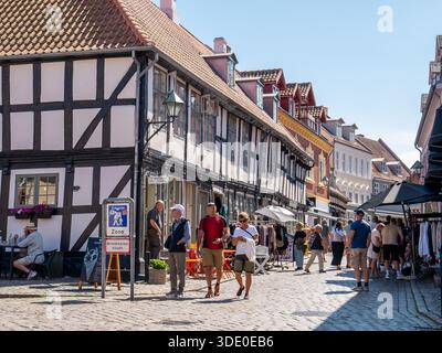 Leute schlendern entlang der kopfsteingepflasterten Einkaufsstraße Adelgade in der Altstadt von Ebeltoft, Jütland, Dänemark Stockfoto