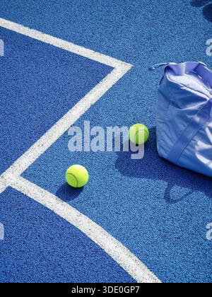 Lavendeltasche und Tennisbälle auf blauem Hartplatz. Eine vertikale Hochwinkelaufnahme einer Sporttasche aus Lavendel und drei neongelben Tennisbälle Stockfoto