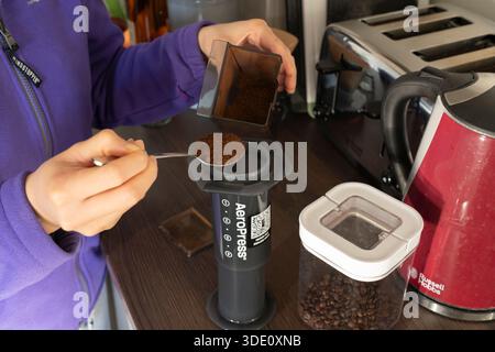 Eine tausendjährige Frau, die frisch gemahlenen Kaffee in eine Aeropress einmischt, um selbstgemachten frisch gebrühten Kaffee in einer Küche in Großbritannien zuzubereiten Stockfoto
