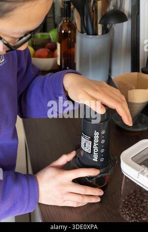 Millennials-Frau, die eine Aeropress niederdrückt, weil sie in einer Küche hausgemachten frisch gebrühten Kaffee gemacht hat, Großbritannien. Konzept: Kaffeesucht, wachsam bleiben Stockfoto