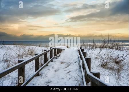 Friedliche Winterszene mit schneebedeckten Holzstegen mit Geländern, die durch Küstendünen in die Ostsee bei Lilaste, Lettland, führen. Stockfoto