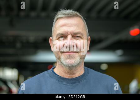 Freundlicher reifer Mann mit grauen Haaren und Bart, der sanft lächelt, während er drinnen vor einem sanft verschwommenen urbanen Hintergrund auf die Kamera blickt. Stockfoto