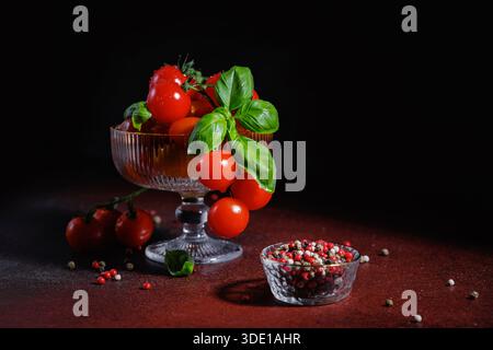 Kirschtomaten und Basilikum in Glasschale auf dunklem Hintergrund für einen gesunden Lebensstil Stockfoto