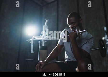 Fitness-Workout im Fitnessstudio. Afroamerikaner Bodybuilder, der im Fitnessstudio Kurzhanteln aufnimmt. Workout Krafttraining Bizepsmuskeln mit Hantel im Fitnessclub. Mann, der Sport treibt. Gesunder Lebensstil Stockfoto