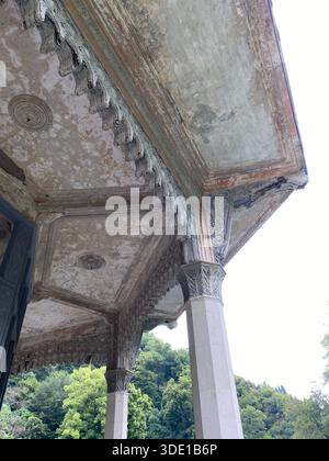Architektonische Details des antiken Gebäudes mit komplizierten Schnitzereien, umgeben von üppigem Grün. Mobiles Foto Stockfoto