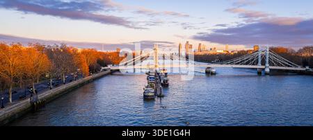 Panoramablick auf die Albert Bridge über die Themse in goldener Stunde, die Chelsea und Battersea verbindet, während die Londoner Skyline leuchtet; für Reisen, Transport, Re Stockfoto