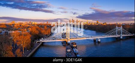Panoramablick auf die Albert Bridge über die Themse in goldener Stunde, die Chelsea und Battersea verbindet, während die Londoner Skyline leuchtet; für Reisen, Transport, Re Stockfoto