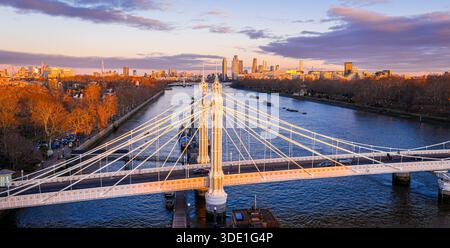 Panoramablick auf die Albert Bridge über die Themse in goldener Stunde, die Chelsea und Battersea verbindet, während die Londoner Skyline leuchtet; für Reisen, Transport, Re Stockfoto