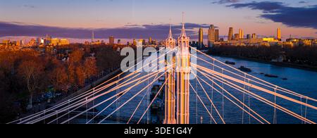 Panoramablick auf die Albert Bridge über die Themse in goldener Stunde, die Chelsea und Battersea verbindet, während die Londoner Skyline leuchtet; für Reisen, Transport, Re Stockfoto