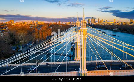 Panoramablick auf die Albert Bridge über die Themse in goldener Stunde, die Chelsea und Battersea verbindet, während die Londoner Skyline leuchtet; für Reisen, Transport, Re Stockfoto