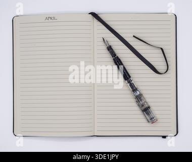 Ein minimalistischer Blick von oben auf ein offenes Notebook mit der Aufschrift April mit einem stilvollen Füllfederhalter für kreatives Schreiben und Organisieren. Stockfoto
