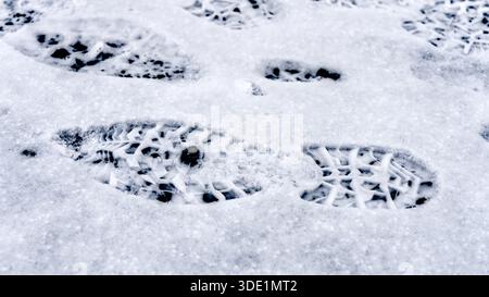Nahaufnahme der Stiefeldrucke im Schnee, die die strukturierte Oberfläche und die winterlichen Details hervorheben. Stockfoto