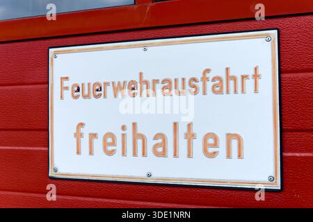 Feuerwehrausgangsschild mit roter Schrift auf weißem Hintergrund, montiert an einer roten Wand Stockfoto