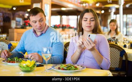 Modernes Paar, das während des Mittagessens im Restaurant Mobiltelefone benutzt Stockfoto