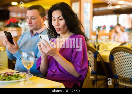 Ein erwachsenes Birazialpaar benutzt während des Mittagessens im Restaurant ein Telefon Stockfoto