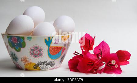 Hühnereier in einer Schüssel neben roten Blumen Stockfoto