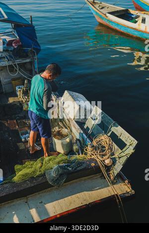 Balikpapan, Indonesien - 8. November 2025. Ein Fischer, der gerade von einem Angelausflug zurückgekehrt ist, steht auf seinem Bootsdeck und sortiert verworrene grüne Netze und Stockfoto