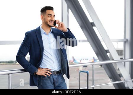 Mobile Kommunikation. Gutaussehender Mann Aus Dem Nahen Osten, Der Auf Dem Handy Am Flughafen Spricht Stockfoto