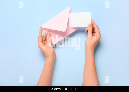 Weibliche Hände mit rosafarbenem Umschlag und leerer Karte auf blauem Hintergrund. Valentinstag-Feier Stockfoto