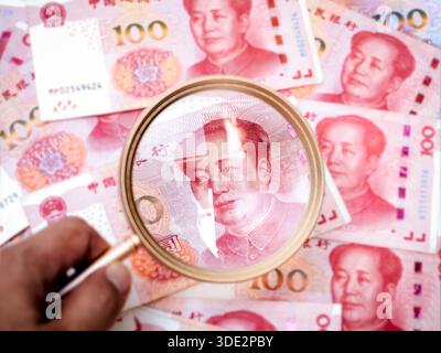 Nahaufnahme chinesischer 100-Yuan-Banknoten mit goldener Lupe, die Mao Zedongs Porträt hervorheben und Chinas Wirtschaftswachstum und Investitionen symbolisieren Stockfoto