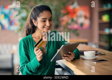 Fröhliche indische Dame Online-Banking, mit digitalen Tablet im Café Stockfoto