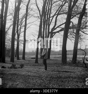 Ein monochromes Archivfoto aus der Sowjetzeit der 1980er Jahre zeigt Kravelis Dmitri Michailowitsch, der zwischen hohen Bäumen in der Nähe des überfluteten „Appendizitis“-Rückwassers in Brusino, Region Donezk, Ukraine UdSSR steht. Er hält eine alte Kamera, bereitet sich auf ein Foto vor oder passt das Objektiv an. Der Hintergrund zeigt das geschwollene Wasser des Seversky Donets River. Dieses ehrliche Porträt zeigt Amateurfotografie und Outdoor-Freizeit im friedlichen Donbass vor dem Krieg und dokumentiert einen ruhigen Moment der Kreativität. Stockfoto