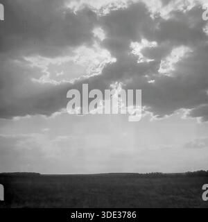 Das monochrome Archivfoto aus den 1970er Jahren der Sowjetzeit zeigt eine atemberaubende Skyscape über den offenen Steppen der Region Donezk, Ukraine UdSSR. Die Sonne verbirgt sich hinter massiven, dunklen Cumulus-Wolken, die einen dramatischen kontrastreichen Effekt mit hellen Silbereinfassungen und krepuskulären Strahlen erzeugen, die in Richtung des dunklen, niedrigen Horizonts strahlen. Dieses stimmungsvolle Bild unterstreicht die Weite des Himmels und die rohe, zeitlose Schönheit der ländlichen Landschaft im friedlichen Donbass vor dem Krieg und zeigt die Pracht der Natur. Stockfoto