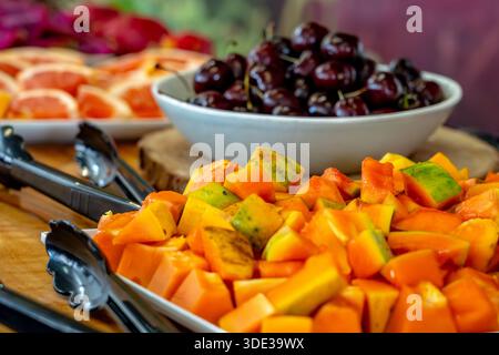 Reife, frische Papaya, geschnitten auf einem Teller mit Kirschen im Hintergrund Stockfoto