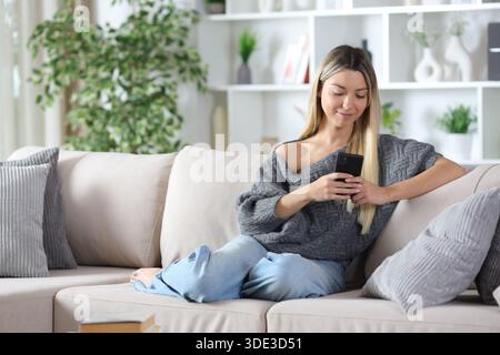 Entspannte Frau zu Hause, die auf einer Couch sitzt und auf einer Couch sitzt Stockfoto