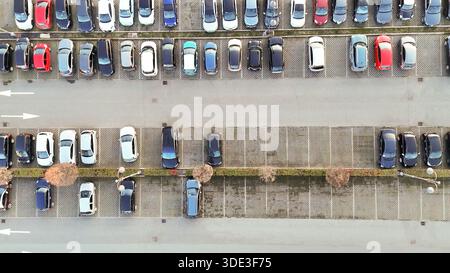 Eine Drohne über der Decke erfasst einen riesigen Parkplatz mit zahlreichen Fahrzeugen, die ordentlich an bestimmten Stellen angeordnet sind, und zeigt die städtische Infrastruktur und tr Stockfoto