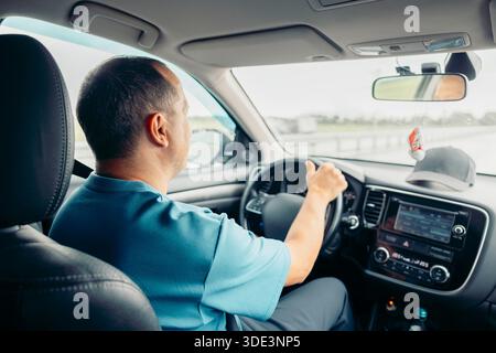 Ein Weißer mittleren Alters mit kurzen Haaren fährt ein Auto auf der Autobahn. Er wirkt konzentriert und entspannt und genießt die Reise. Stockfoto